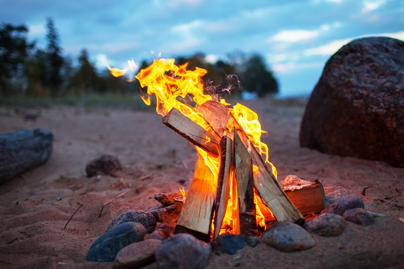 A beach campfire burning at dusk on the red sand shore