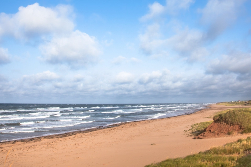 Waves rolling onto a wide sandy beach with red dunes on PEI